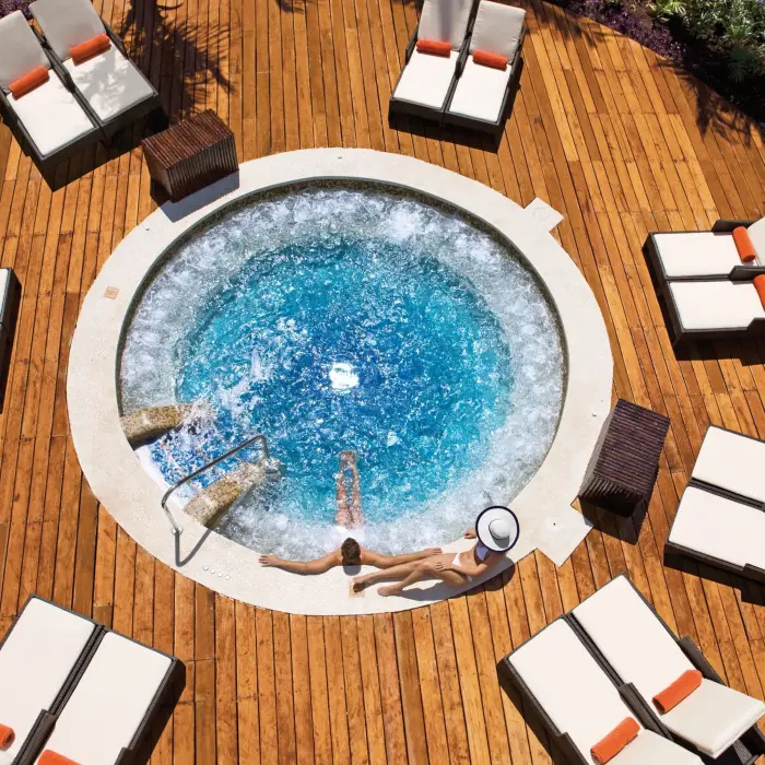 Circular outdoor whirlpool surrounded by sun loungers on a wooden deck.