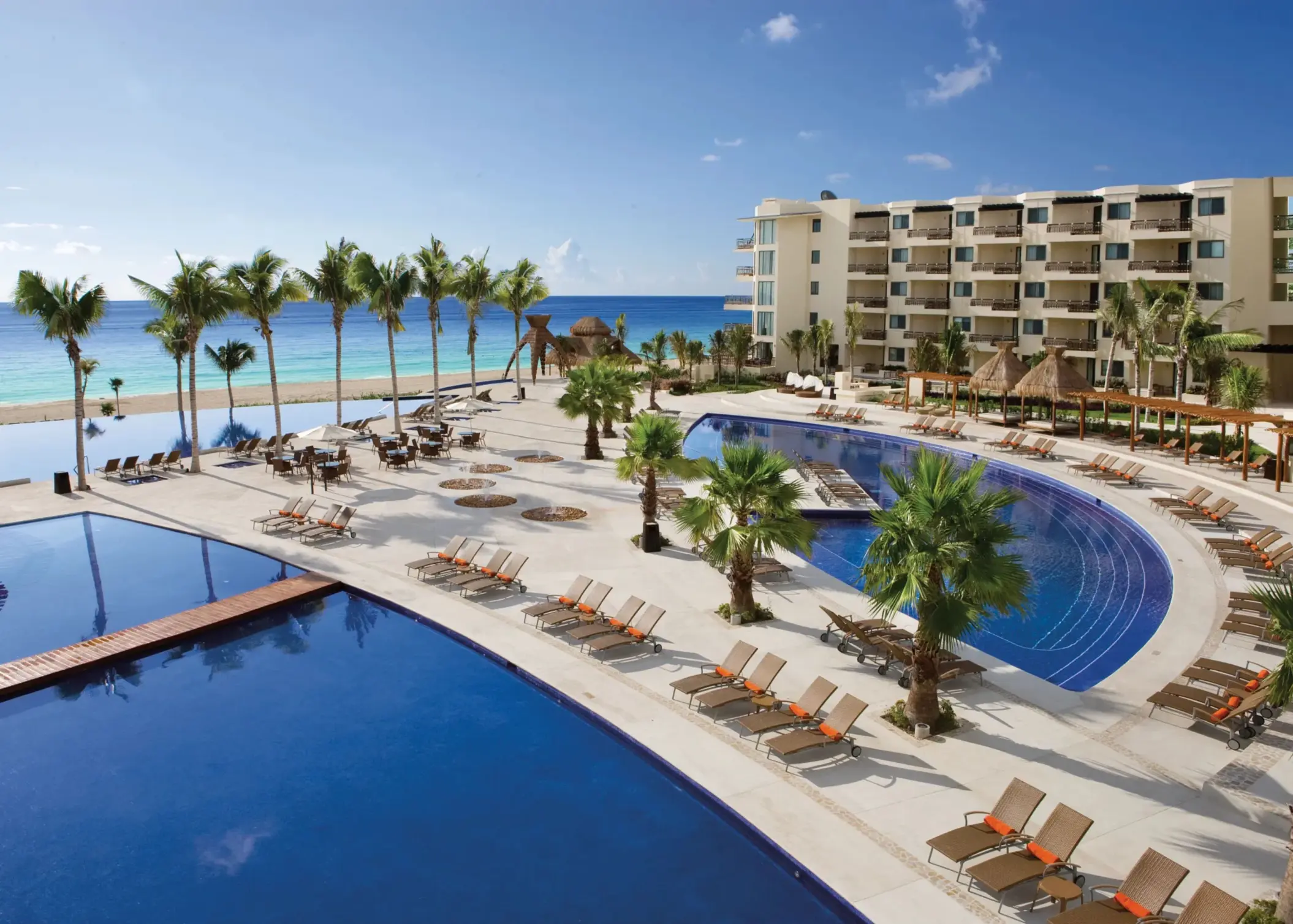Large beachfront pool area with sun loungers, palm trees and ocean views.
