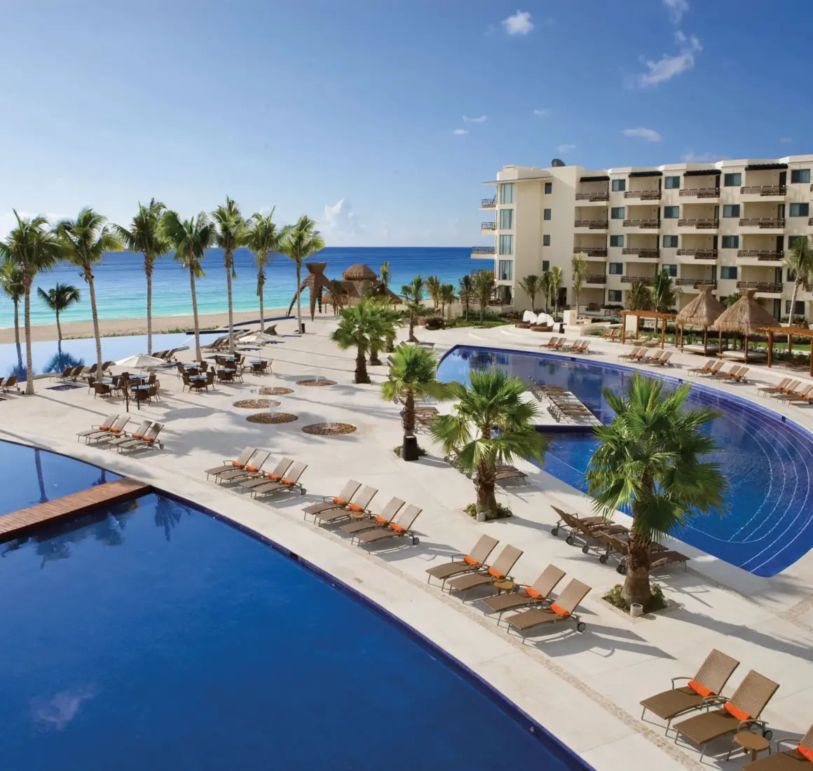 Large beachfront pool area with sun loungers, palm trees and ocean views.