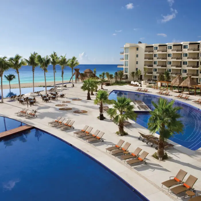 Large beachfront pool area with sun loungers, palm trees and ocean views.