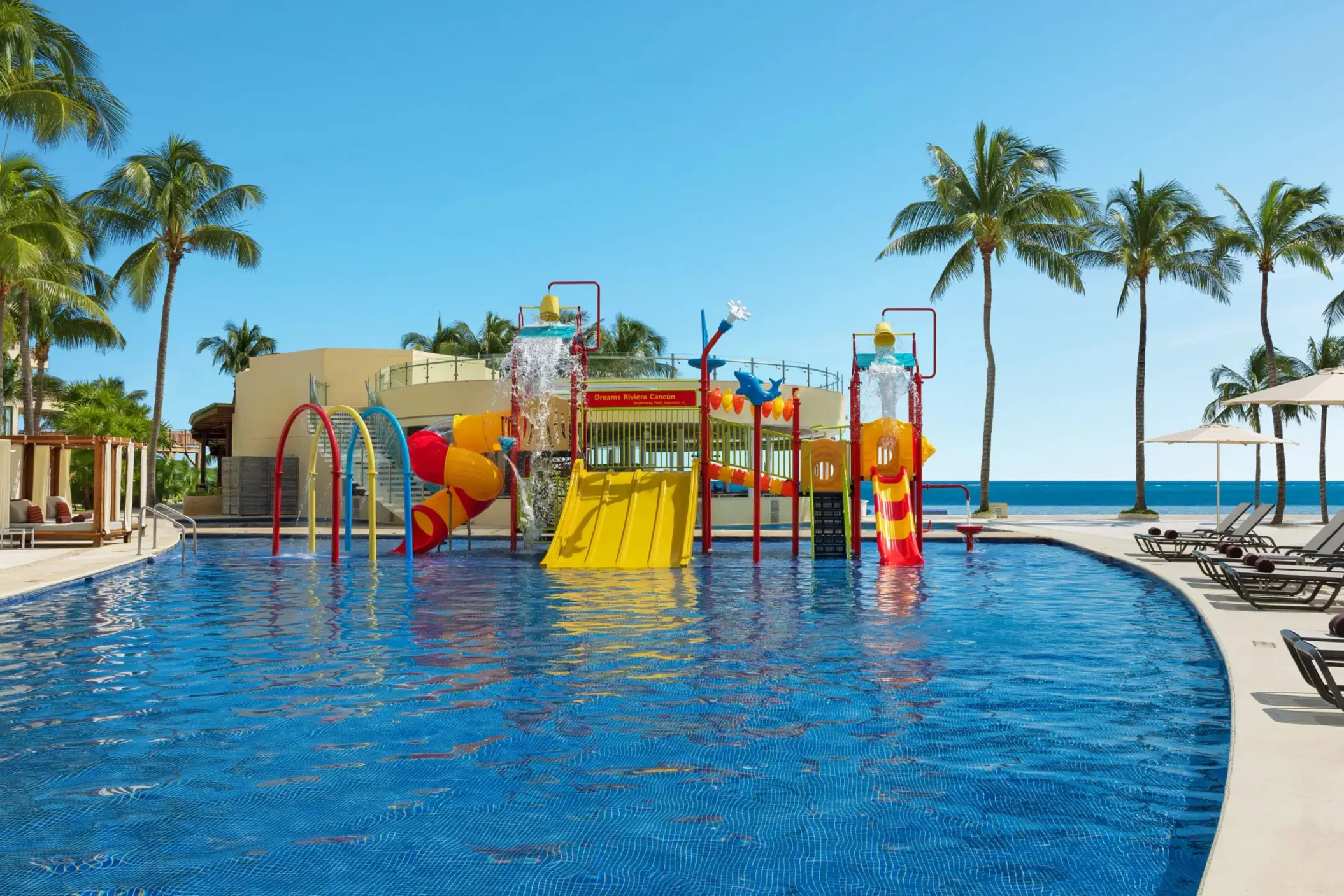 Colorful beachfront waterpark with slides, splash buckets, and kids’ play features at Dreams Riviera Cancun Resort.