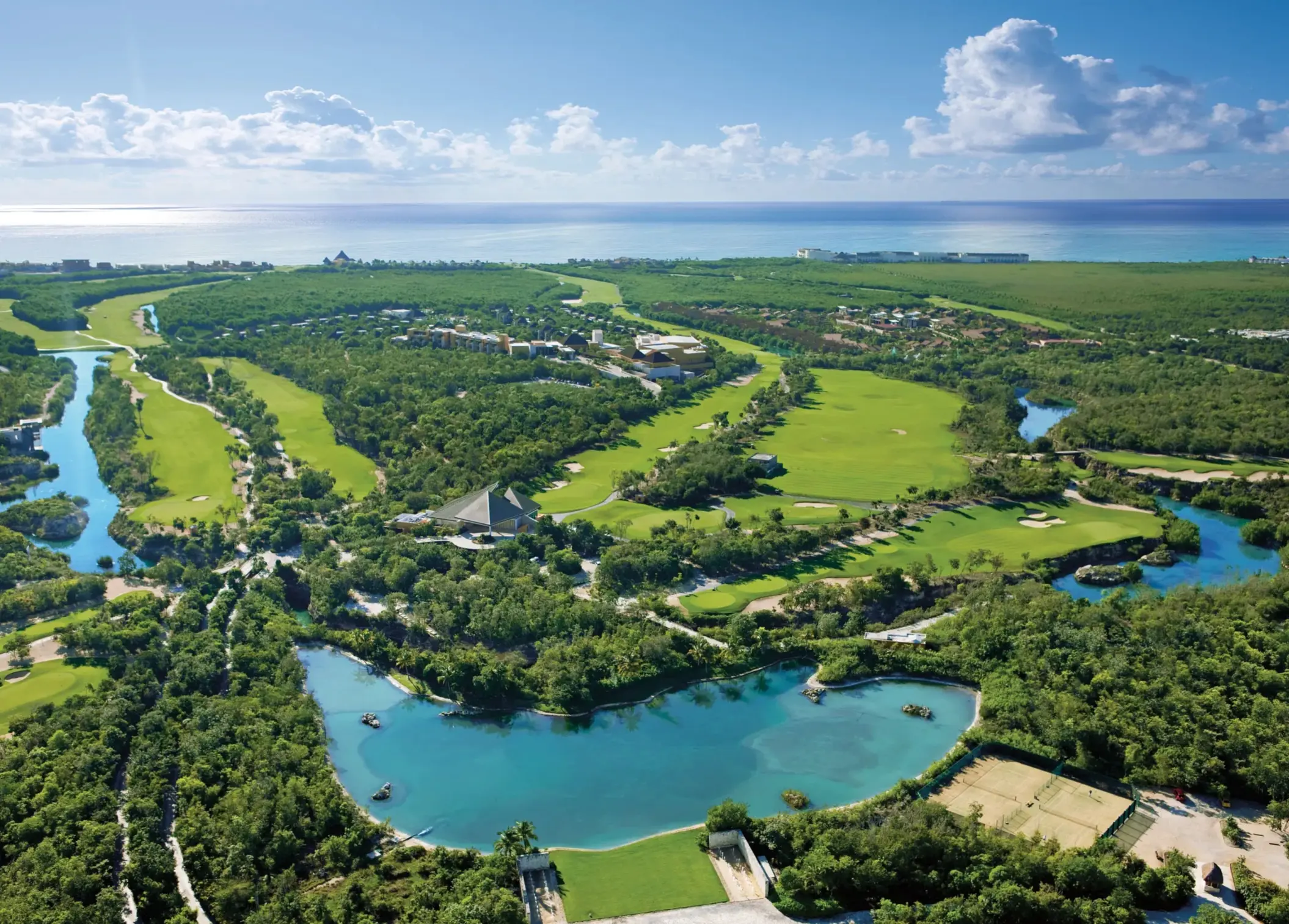 Aerial view of lush Camaleón golf course with waterways and greenery near the ocean.