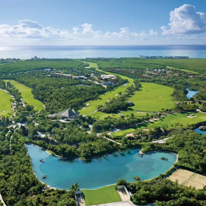 Aerial view of lush Camaleón golf course with waterways and greenery near the ocean.