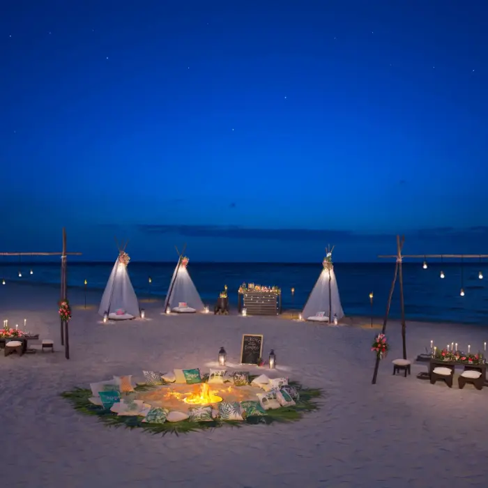 Magical beachfront event setup with teepee tents and firepit under stars.
