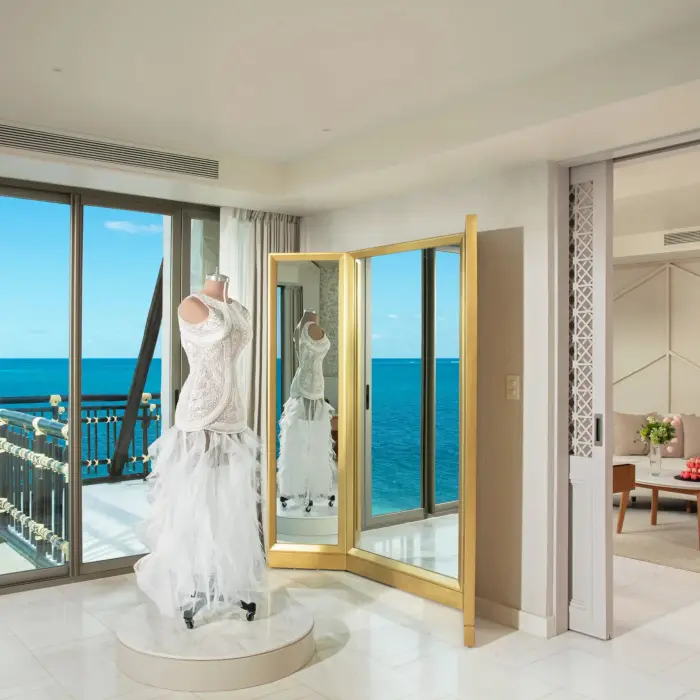Bridal suite fitting room with wedding dress display and ocean backdrop through full-length windows.