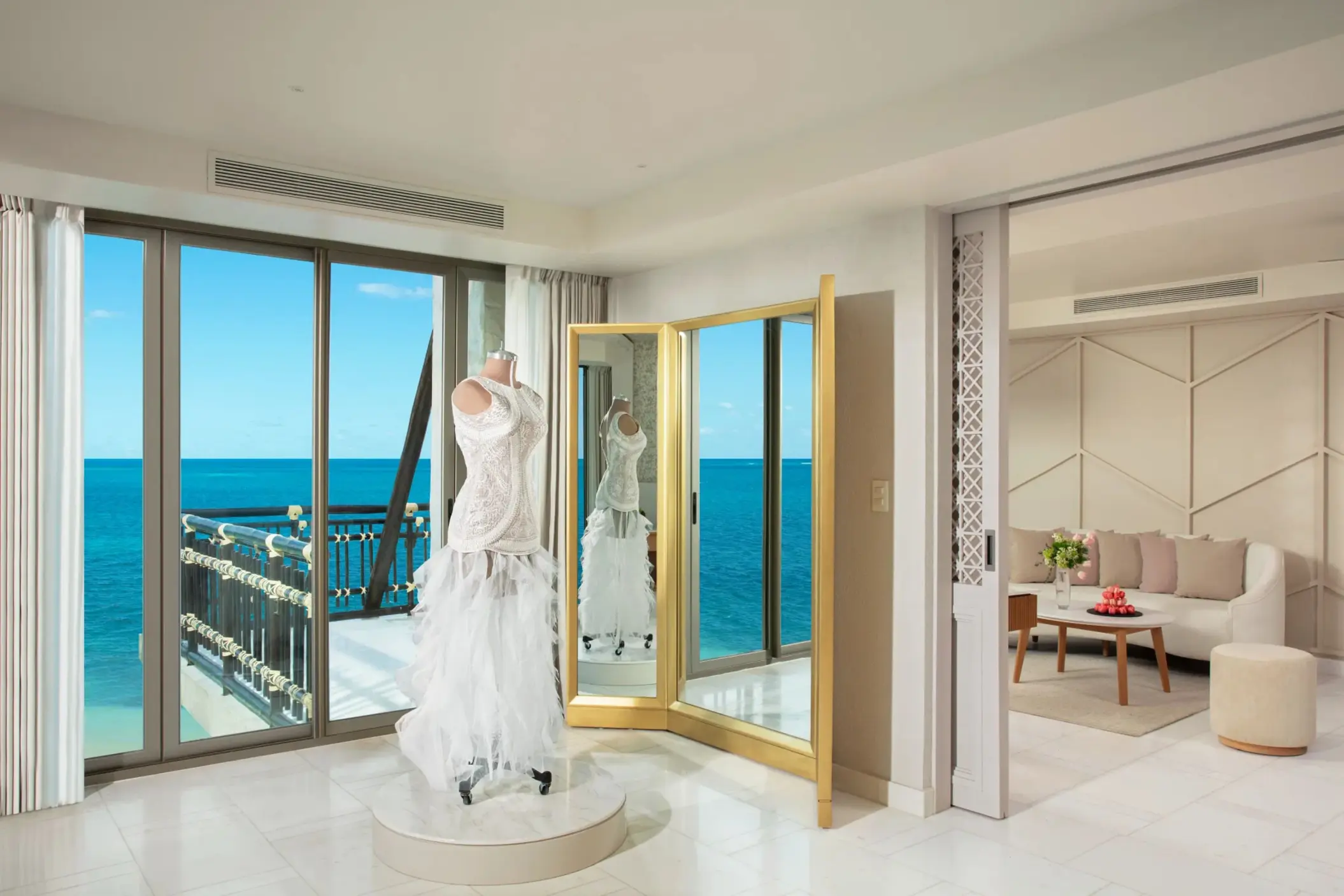 Bridal suite fitting room with wedding dress display and ocean backdrop through full-length windows.