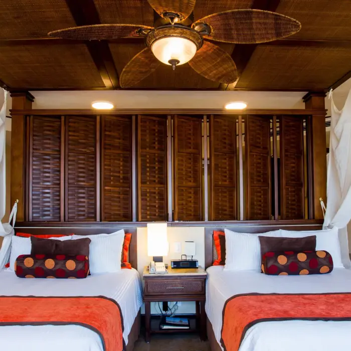 Accessible premium deluxe room with double beds, ceiling fan, and cozy tropical decor.