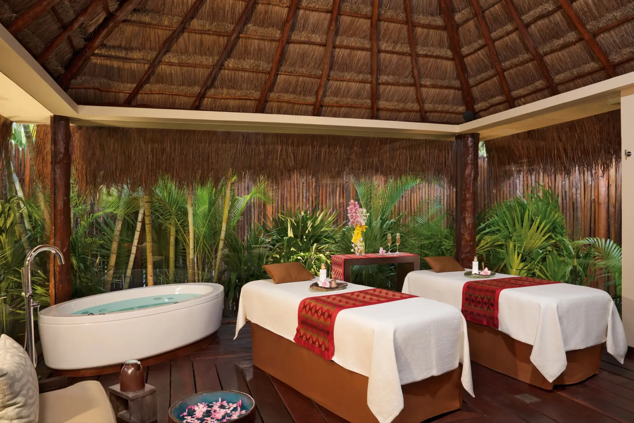 Outdoor spa cabin with two massage tables, lush greenery, and rustic thatched roof at Dreams Riviera Cancun.