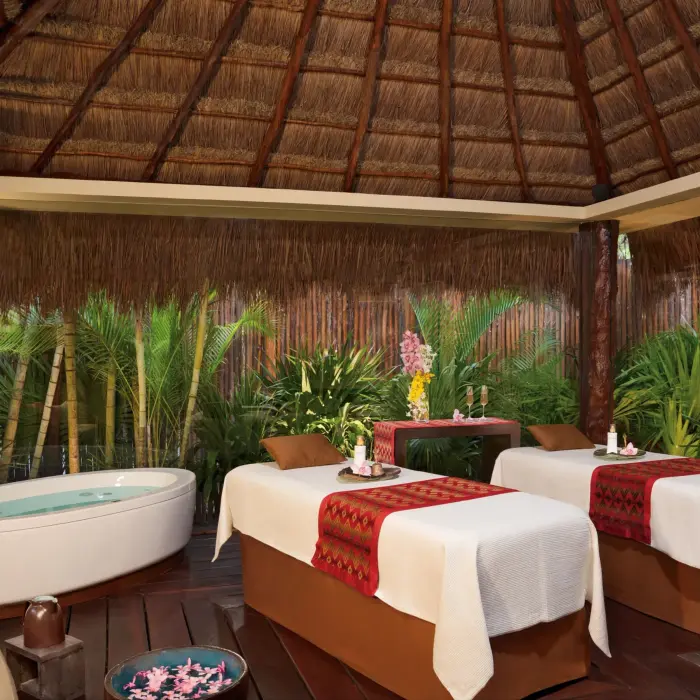Outdoor spa cabin with two massage tables, lush greenery, and rustic thatched roof at Dreams Riviera Cancun.