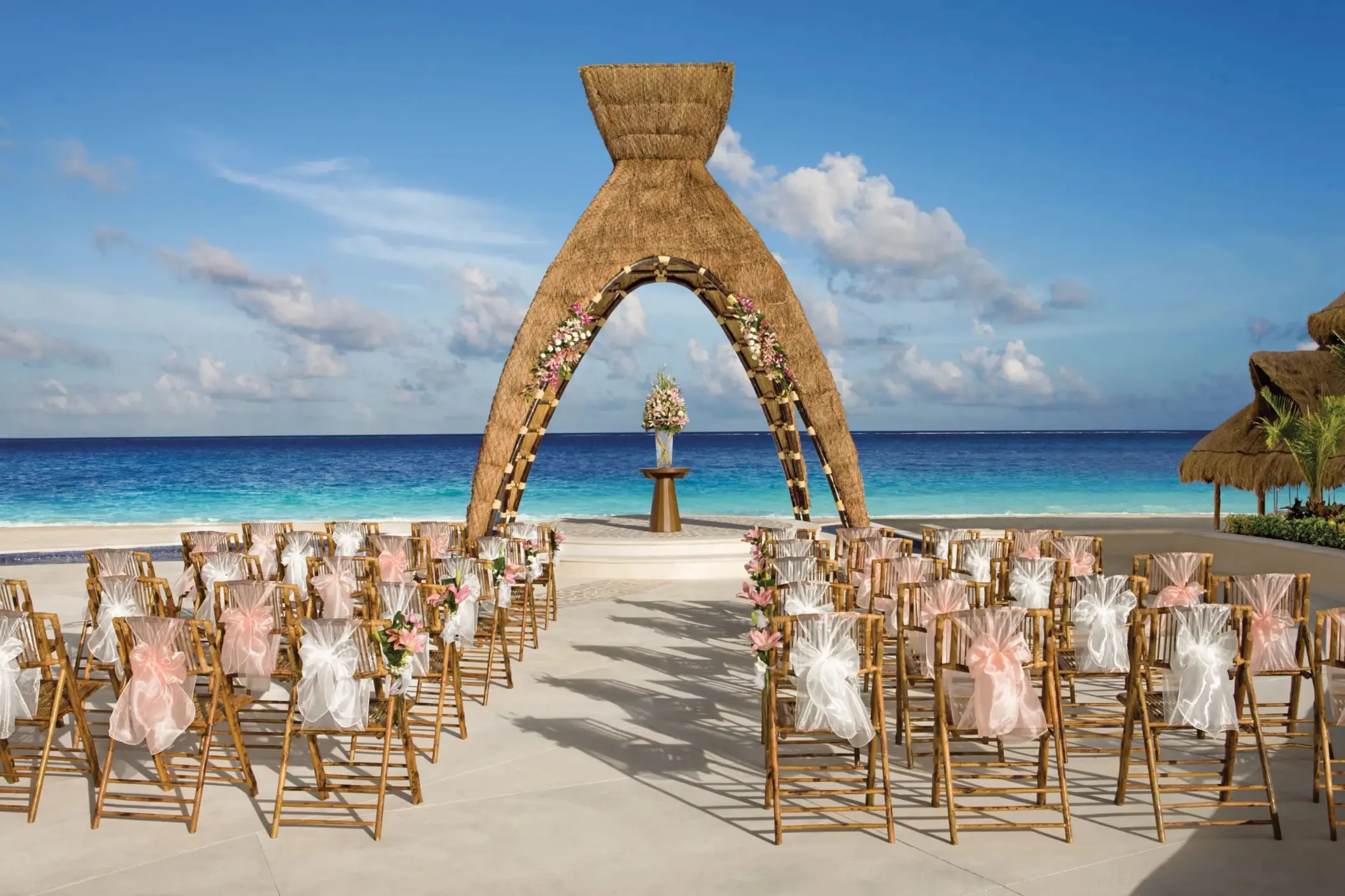 Beachfront wedding setup with floral arch and guest chairs facing the ocean.