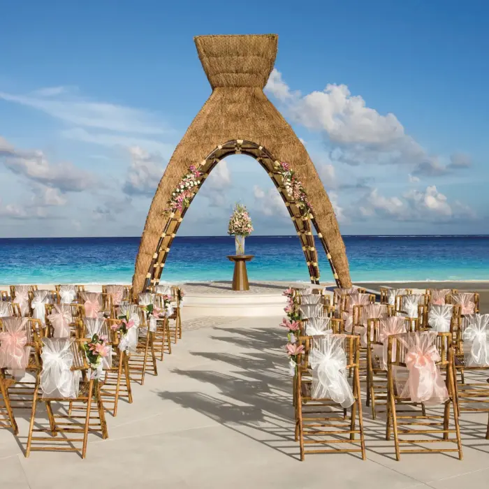 Beachfront wedding setup with floral arch and guest chairs facing the ocean.