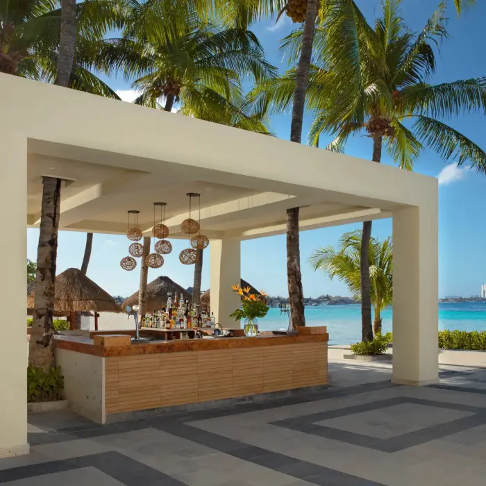 Outdoor beach bar under modern canopy surrounded by palm trees and ocean view.