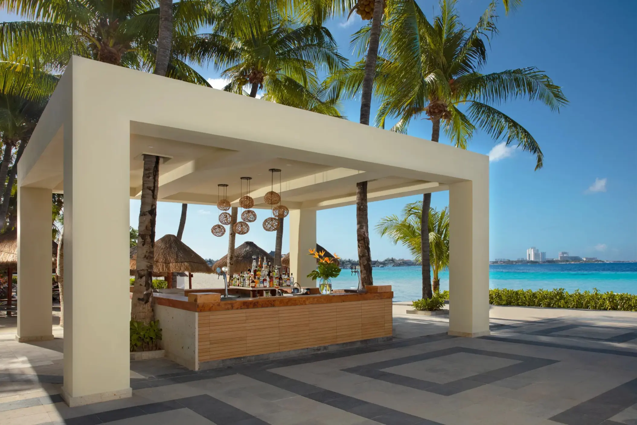 Outdoor beach bar under modern canopy surrounded by palm trees and ocean view.