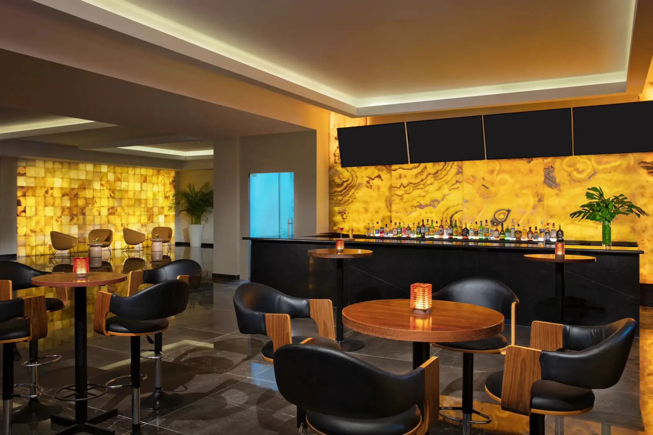 Indoor cocktail bar with amber-colored backlit wall and elegant black seating.