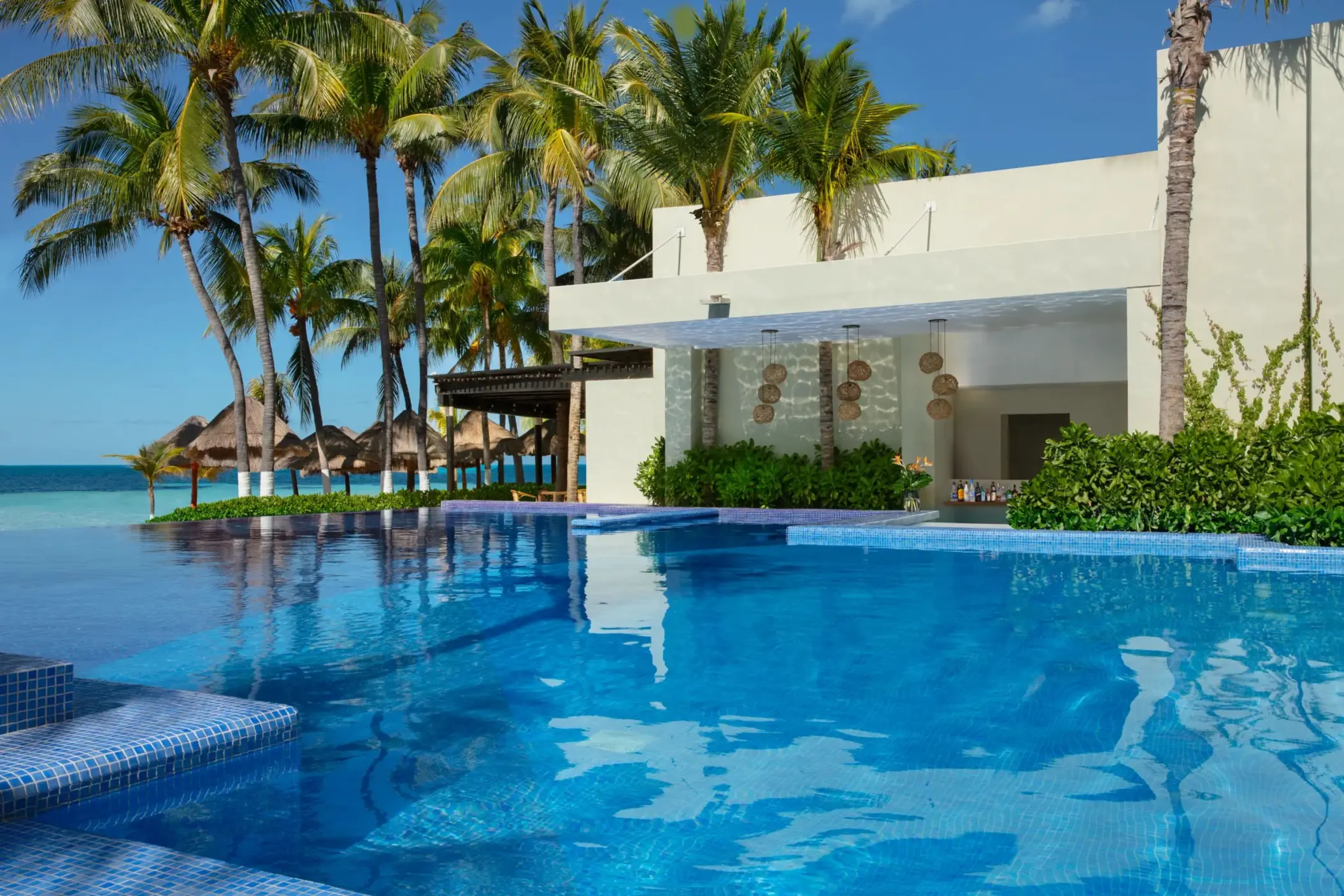 Swim-up bar in infinity pool surrounded by tropical greenery and ocean breeze.