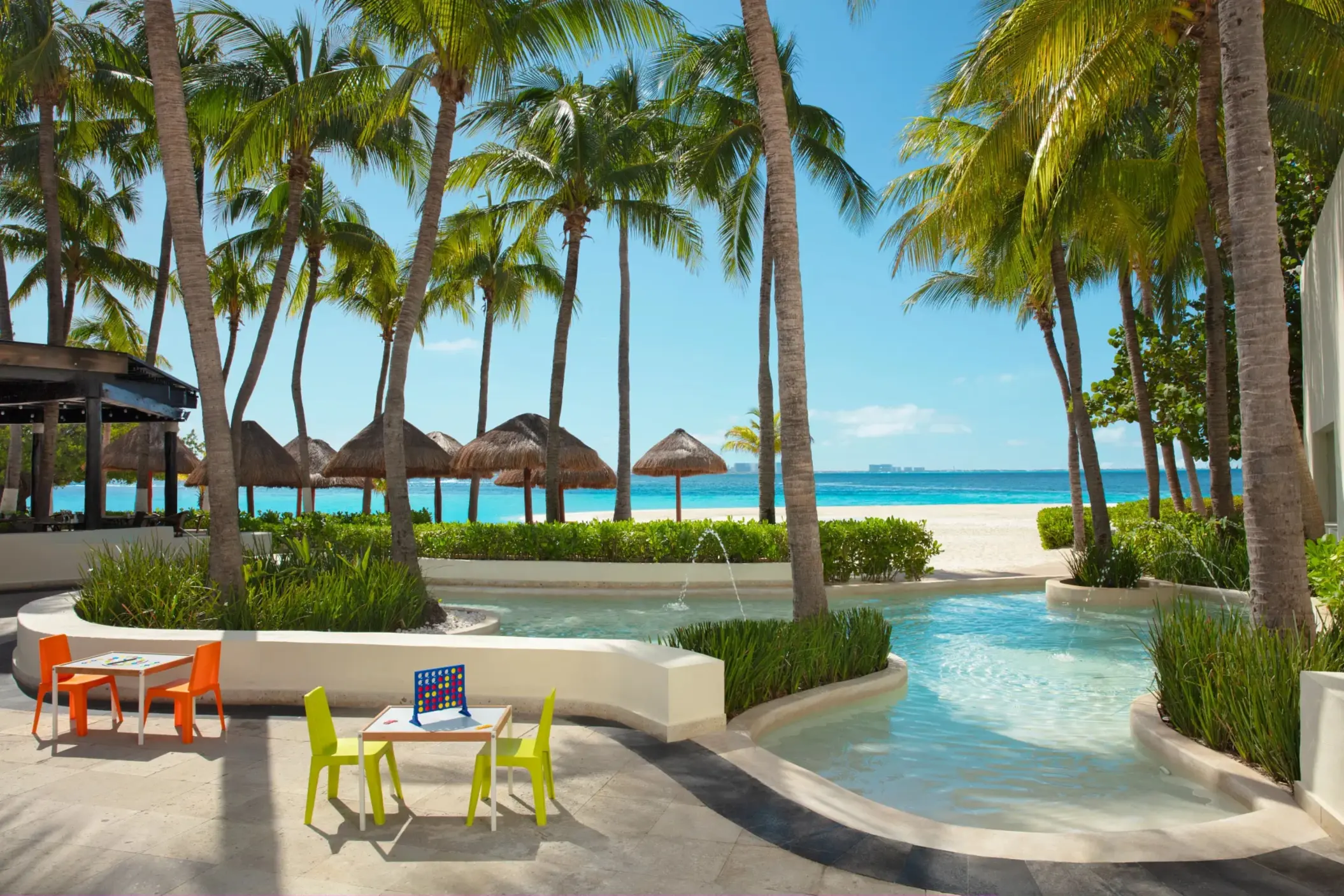 Kid-friendly splash area with games and mini tables surrounded by palm trees.