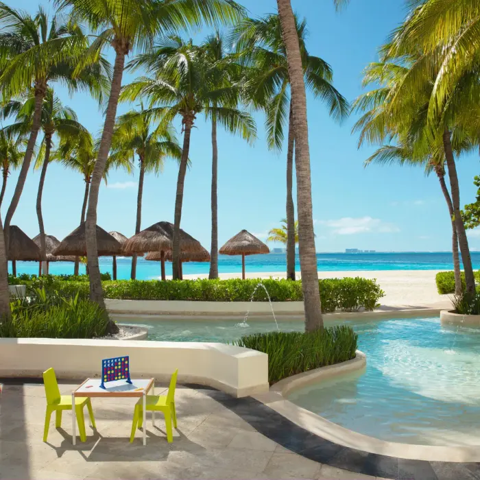 Kid-friendly splash area with games and mini tables surrounded by palm trees.