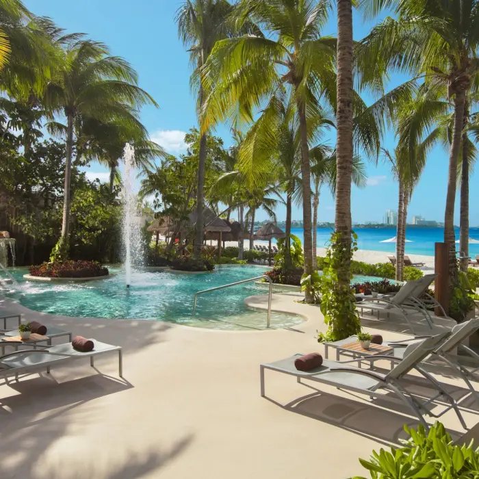 Lush tropical pool area at Dreams Sands Cancun with a central water fountain and ocean backdrop.