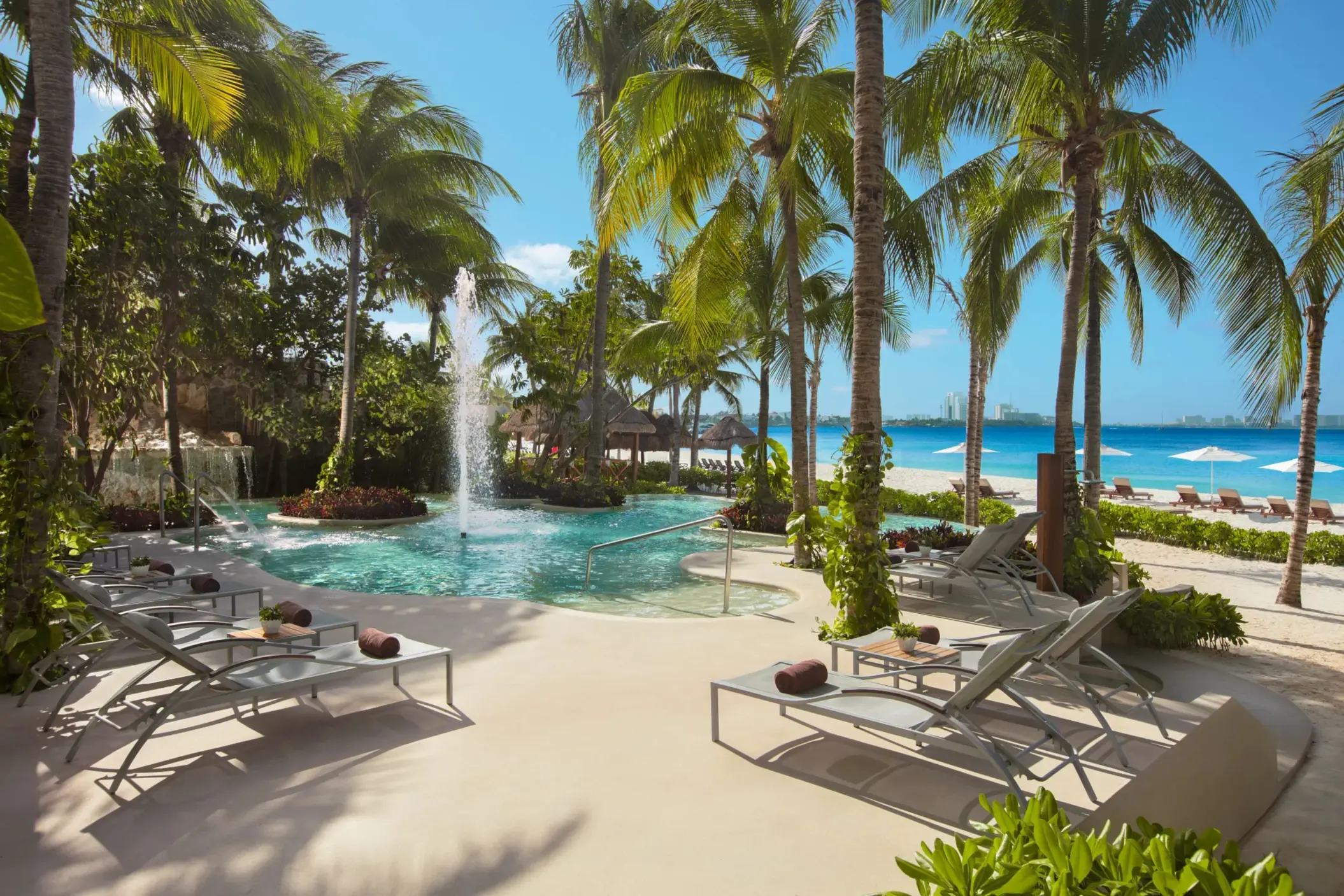 Lush tropical pool area at Dreams Sands Cancun with a central water fountain and ocean backdrop.