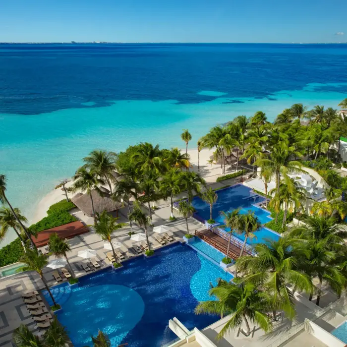Aerial view of multiple pools lined with palm trees and loungers, steps away from the Caribbean Sea.