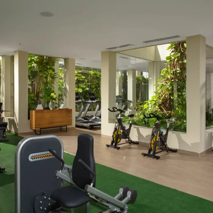Modern fitness center with cardio machines, weights, and greenery views through floor-to-ceiling windows.