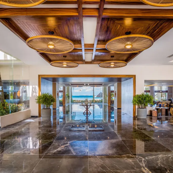 Sleek lobby with glossy marble floors, wood ceiling accents, and a direct view of the beach in the distance.
