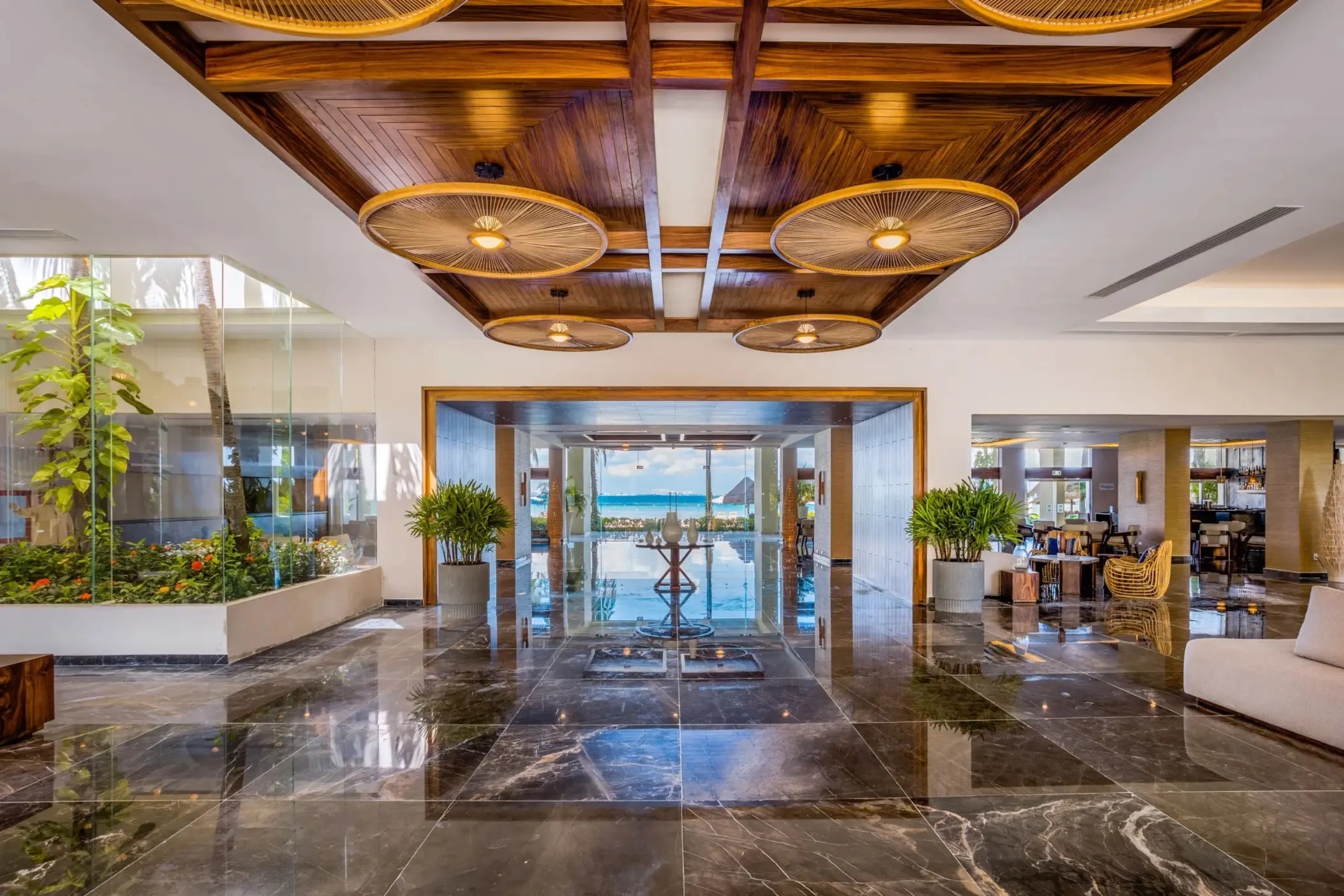 Sleek lobby with glossy marble floors, wood ceiling accents, and a direct view of the beach in the distance.
