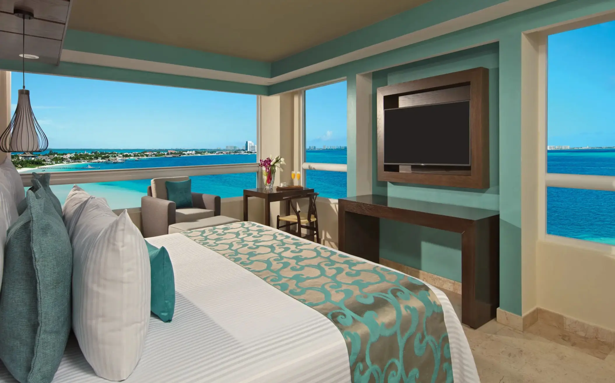 Corner suite with panoramic windows, ocean views, and a flat-screen TV beside the bed.