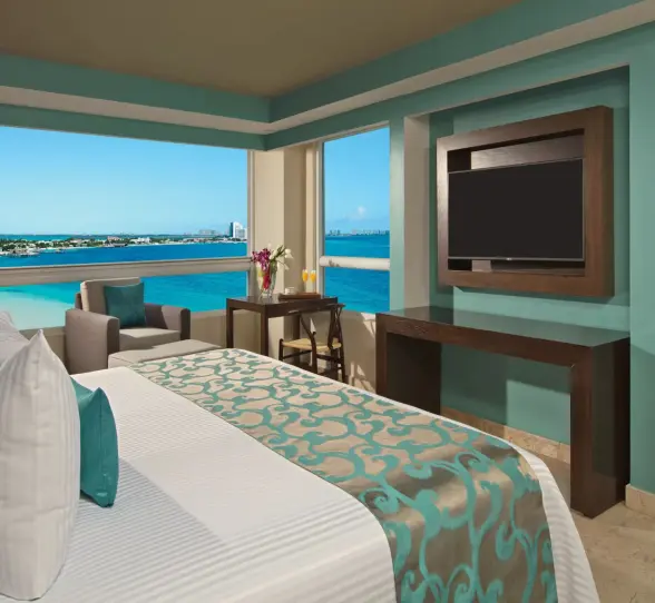 Corner suite with panoramic windows, ocean views, and a flat-screen TV beside the bed.