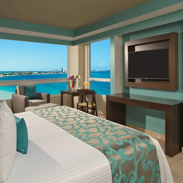 Corner suite with panoramic windows, ocean views, and a flat-screen TV beside the bed.