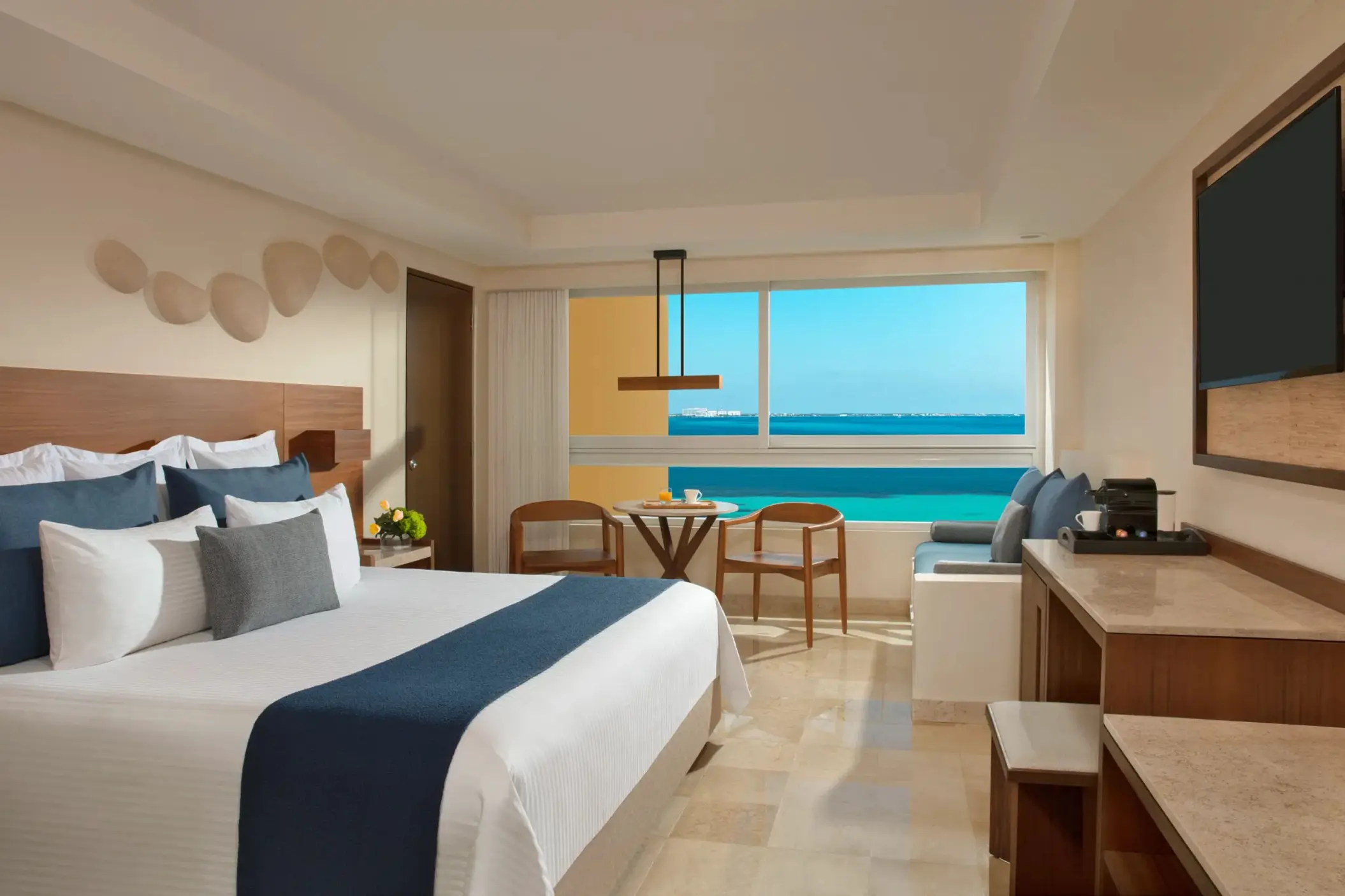 Oceanview room with king bed, modern wooden desk, blue seating bench, and a breakfast setup by the window.