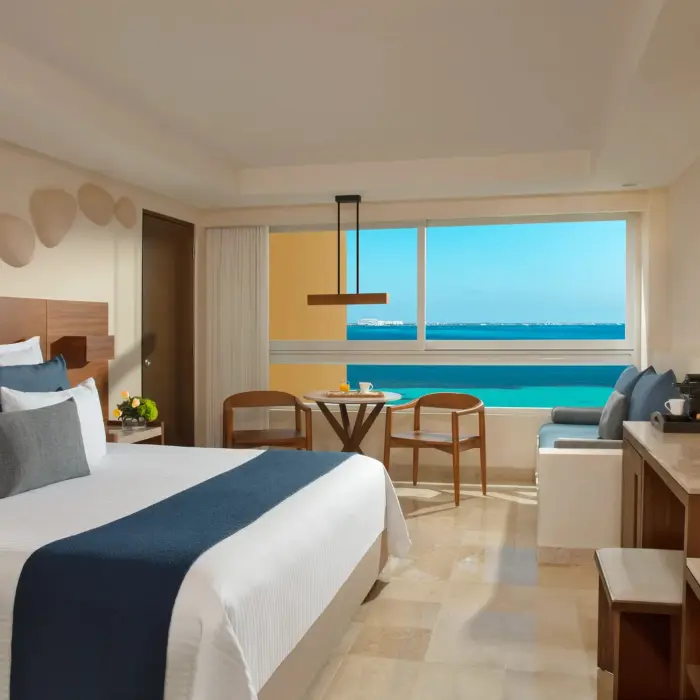 Oceanview room with king bed, modern wooden desk, blue seating bench, and a breakfast setup by the window.