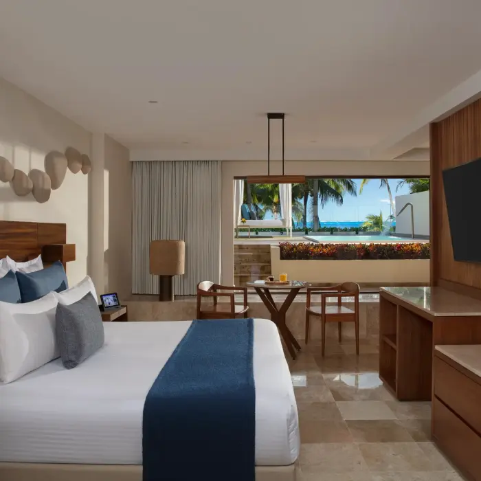 Upscale beachfront suite with king bed, oceanfront terrace, modern TV setup, and a warm wood-accented interior.