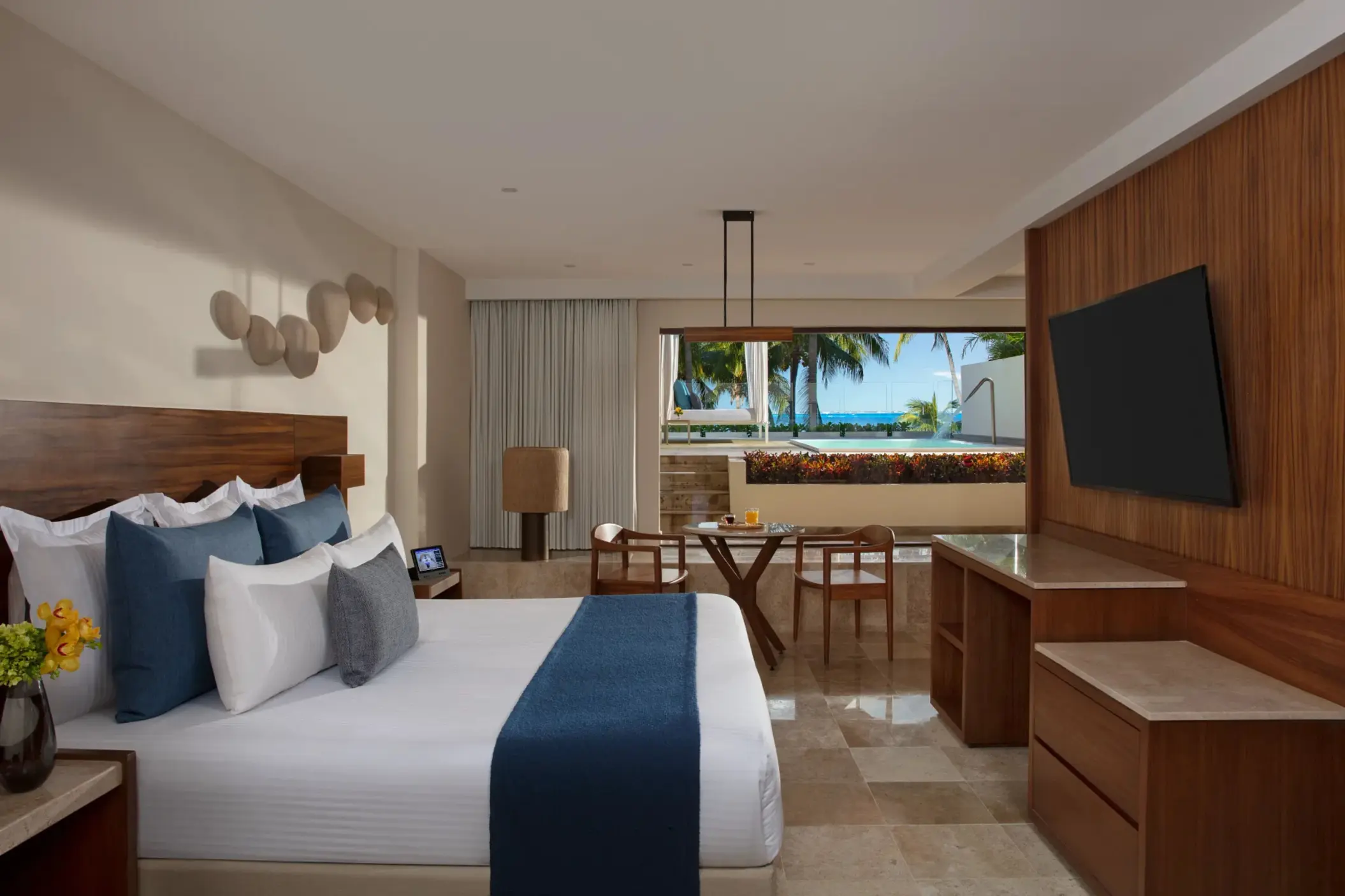 Upscale beachfront suite with king bed, oceanfront terrace, modern TV setup, and a warm wood-accented interior.
