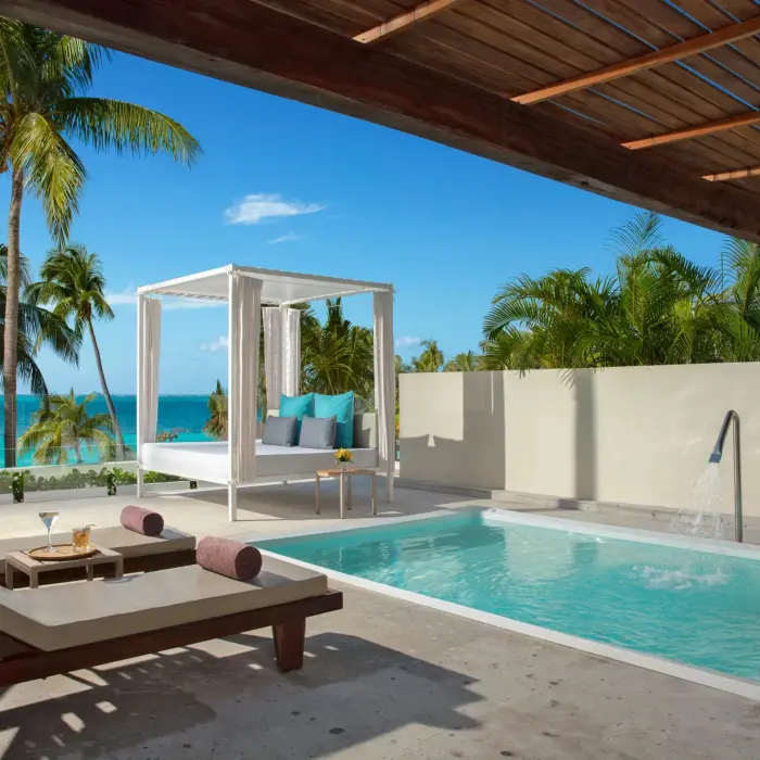 Private terrace with sun loungers, daybed, and plunge pool framed by palm trees and a clear Caribbean view.