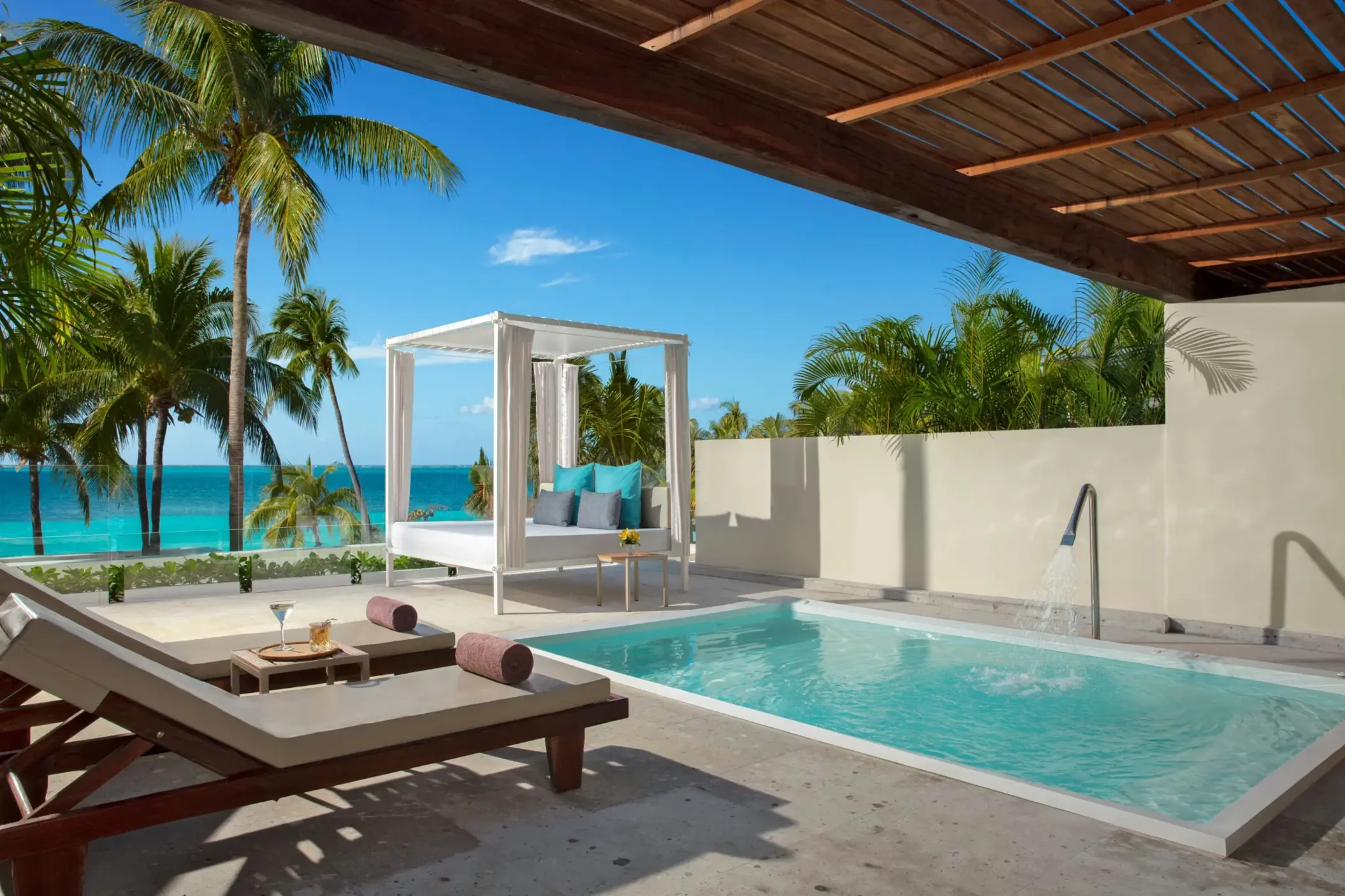 Private terrace with sun loungers, daybed, and plunge pool framed by palm trees and a clear Caribbean view.