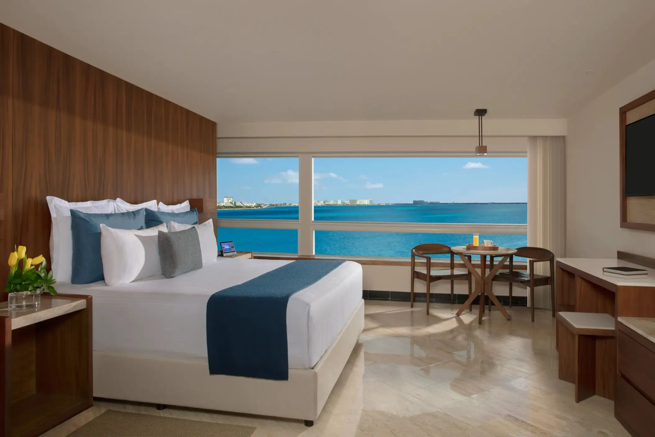 Oceanfront suite with king bed, wood panel accents, work desk, and panoramic views from wide corner windows.