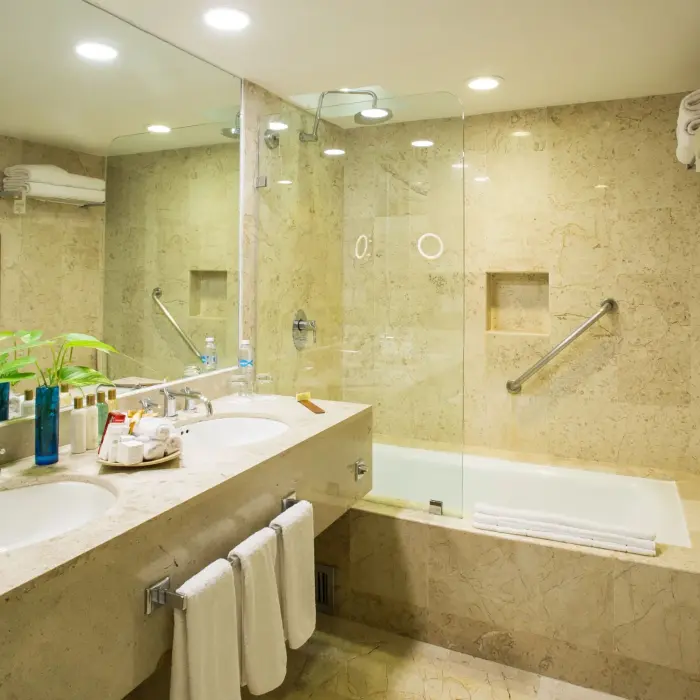 Marble bathroom with glass walk-in shower, tub, dual vanity, and towel racks under soft ceiling lighting.