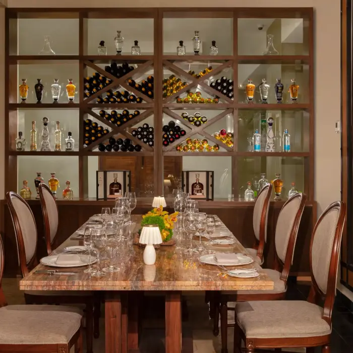 Refined wine cellar dining room with marble table, plush chairs, and backlit shelves of bottles and barrels.