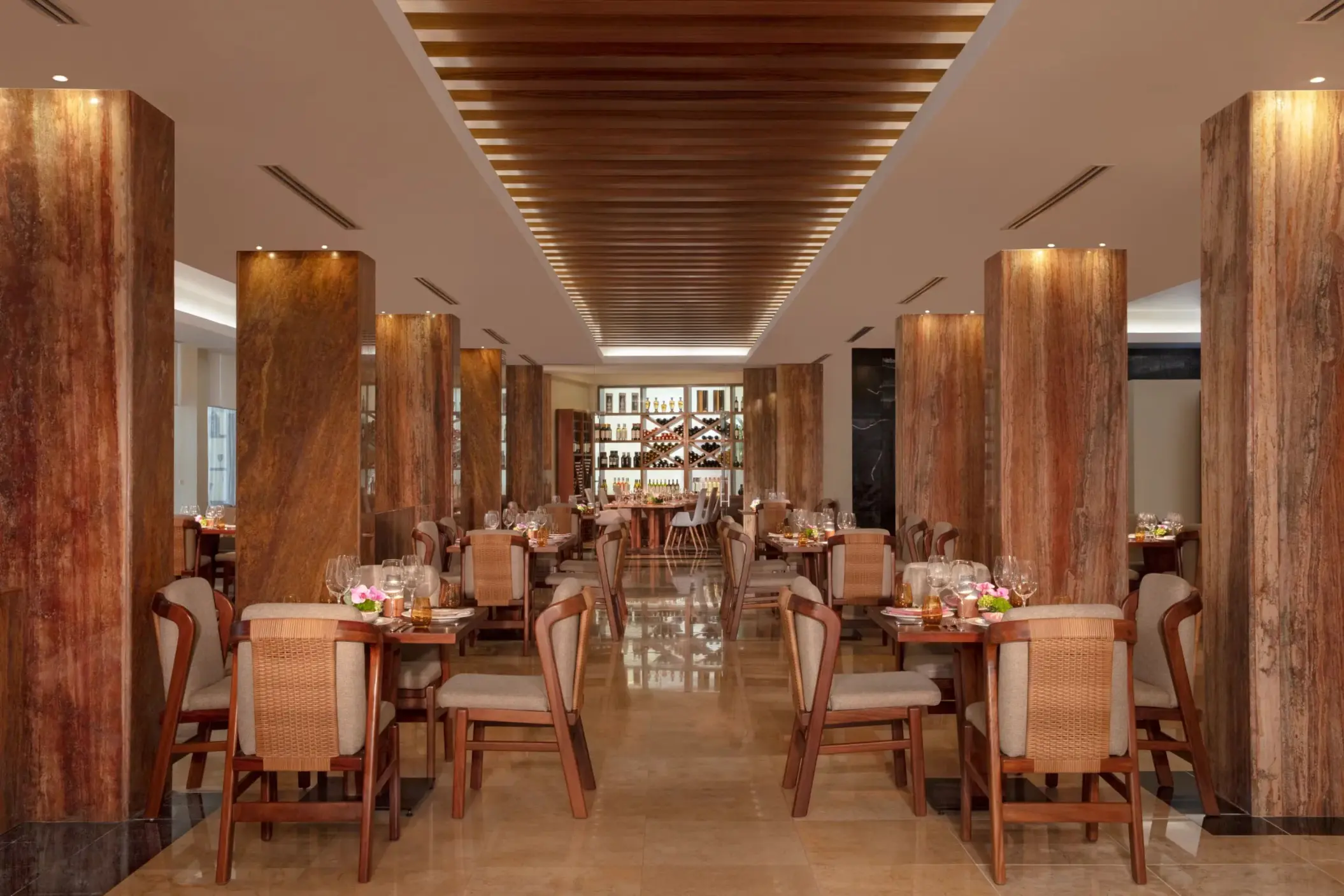 Elegant restaurant interior with polished floors, wood columns, and woven-back chairs arranged in rows.