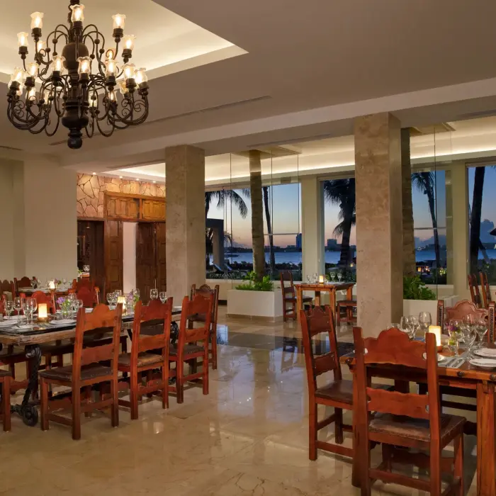 Gaucho Grill’s rustic dining room with warm lighting, wood furniture, and sunset ocean views.