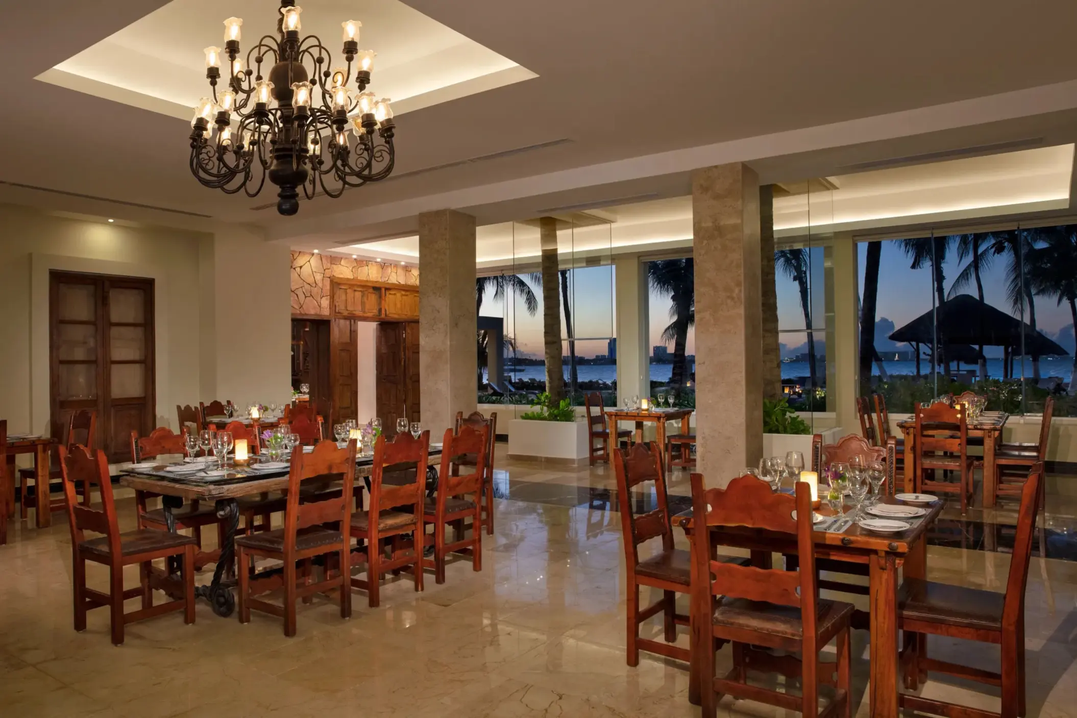 Gaucho Grill’s rustic dining room with warm lighting, wood furniture, and sunset ocean views.