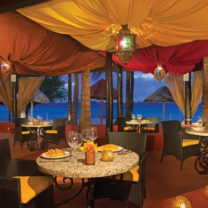 Romantic Olio beachfront dining under colorful canopy with ocean view and candlelit tables.