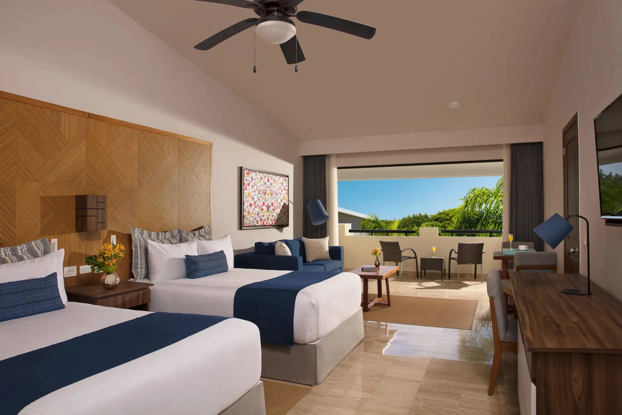 Bright double-bed family room with ceiling fan, cozy sitting area, and view of a private furnished terrace.