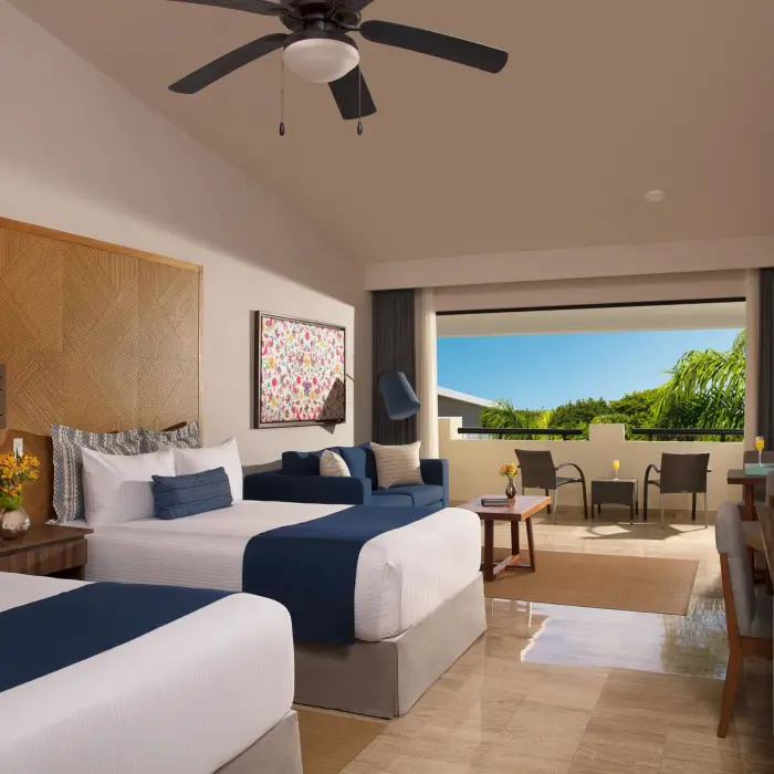 Bright double-bed family room with ceiling fan, cozy sitting area, and view of a private furnished terrace.