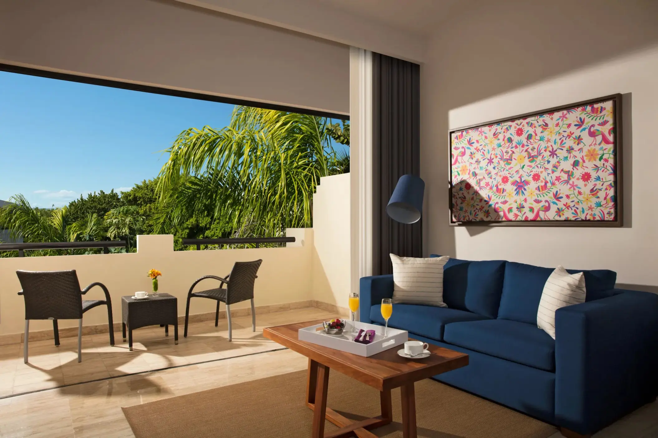 Spacious suite with private balcony, two chairs and table, tropical views, and comfortable seating inside.