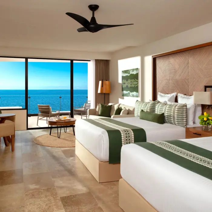 Oceanfront room with two double beds, tropical wood accents, and a balcony overlooking the sea.