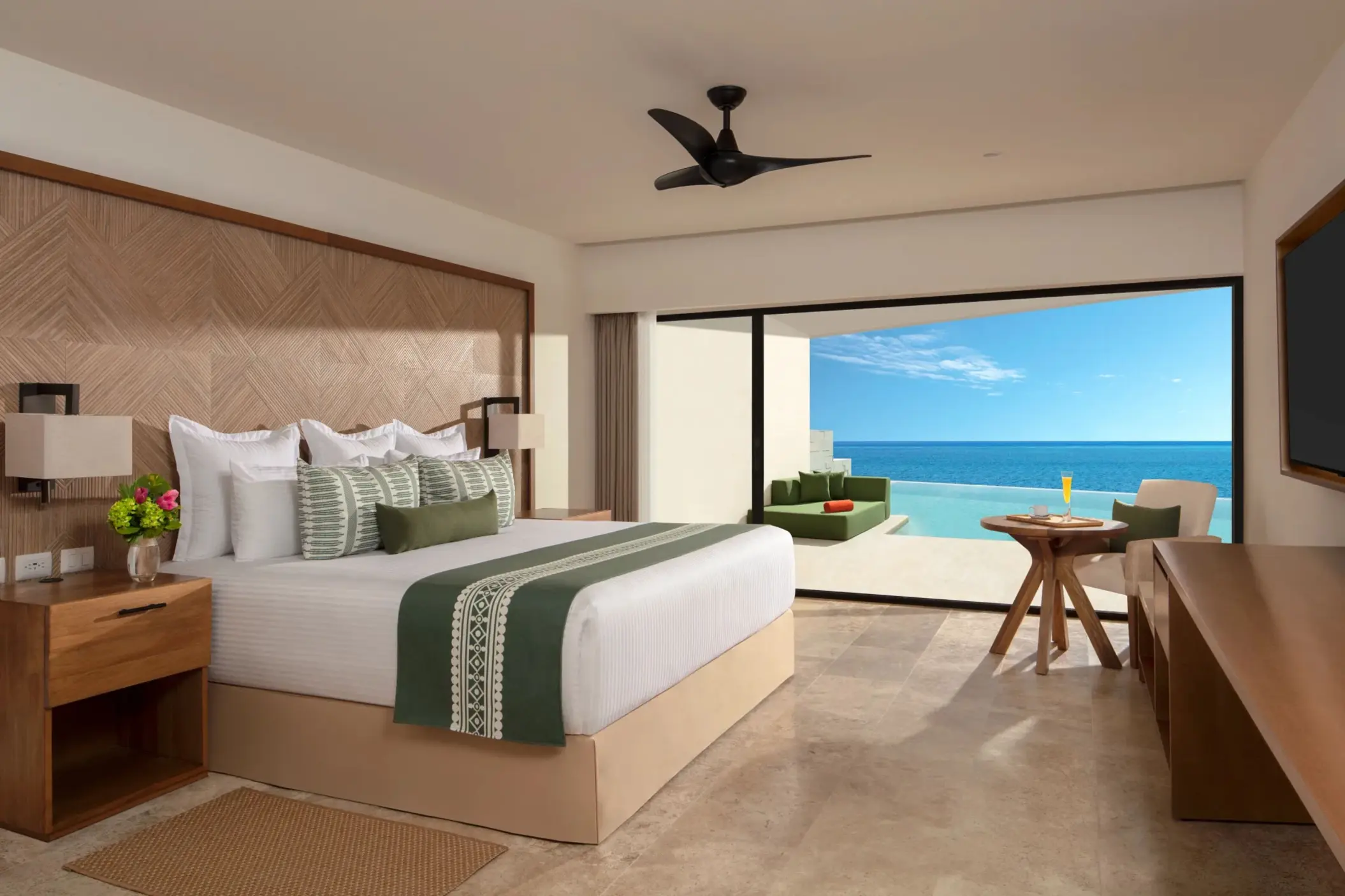 Elegant suite with ocean views, outdoor lounge area, and king bed with textured wood headboard.