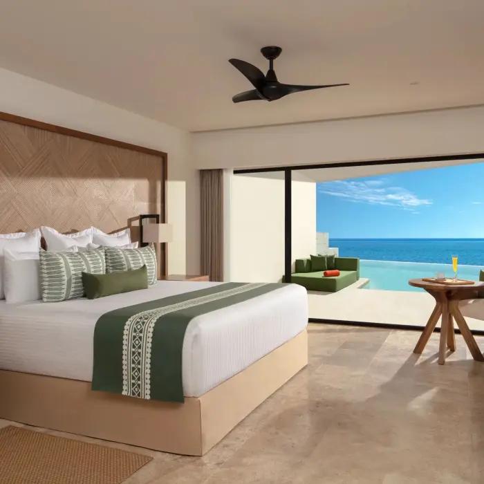 Elegant suite with ocean views, outdoor lounge area, and king bed with textured wood headboard.