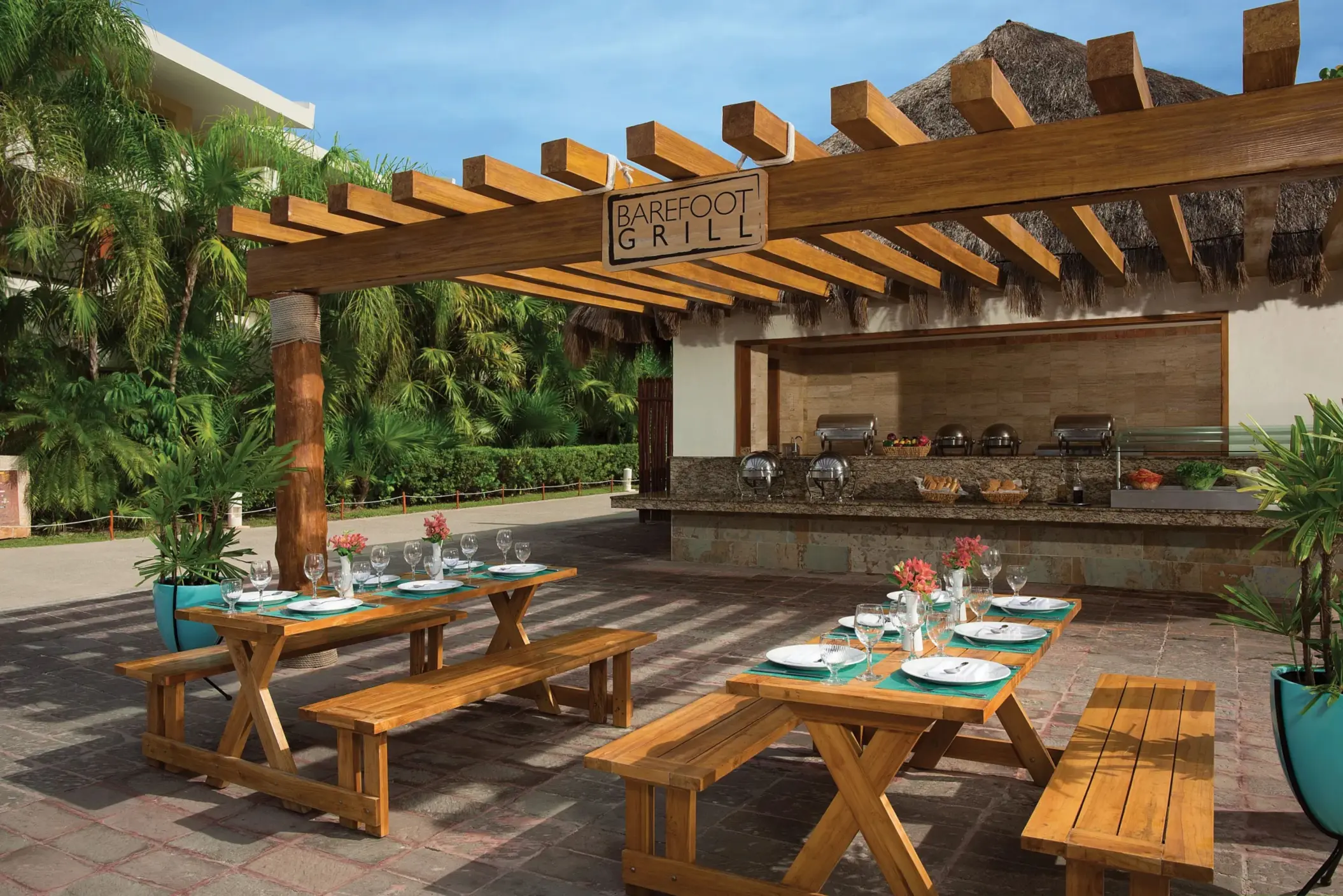 Outdoor Barefoot Grill with picnic tables, wooden pergola, and tropical palm surroundings.
